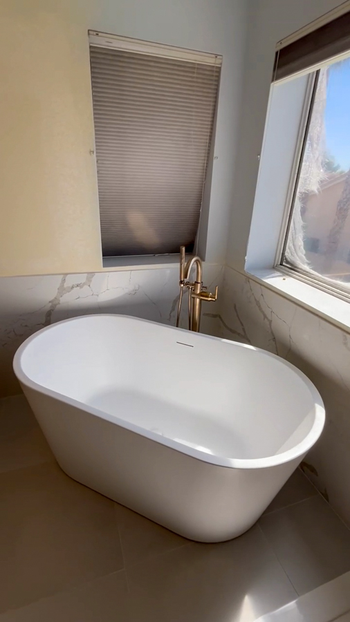 Freestanding soaking tub with a quartz surround and brushed-gold filler by Orange Cactus Remodeling