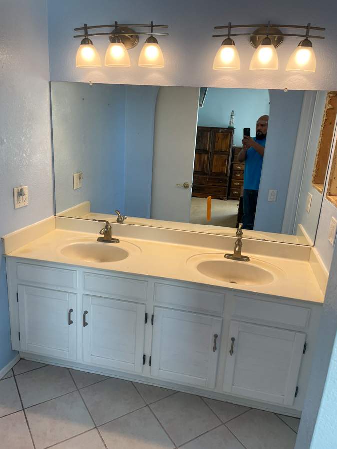 A dated double vanity with a light bar before an Orange Cactus bathroom remodel, the kind of fixture left in place for decades